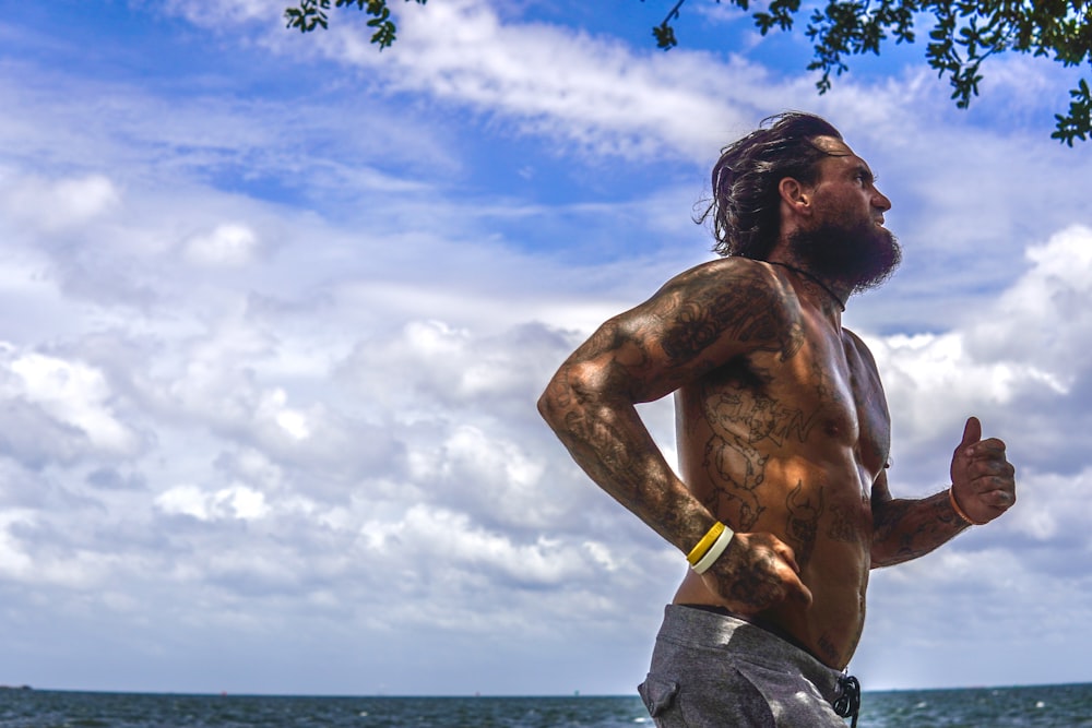 a man with a beard and no shirt running on the beach