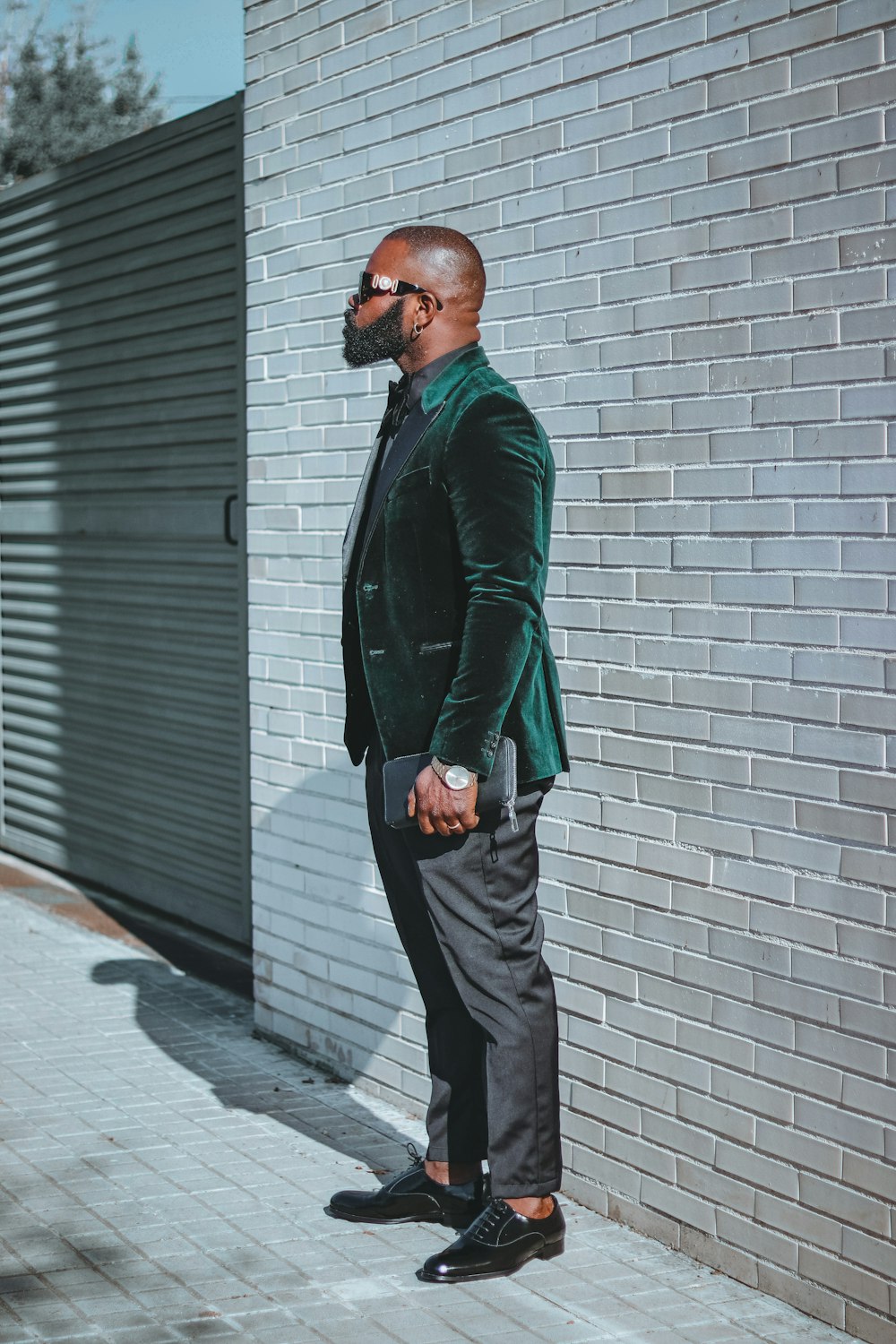 a man in a suit and sunglasses standing in front of a brick wall