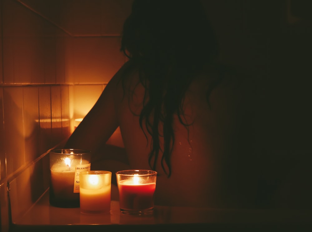 a woman sitting in front of candles in a bathroom