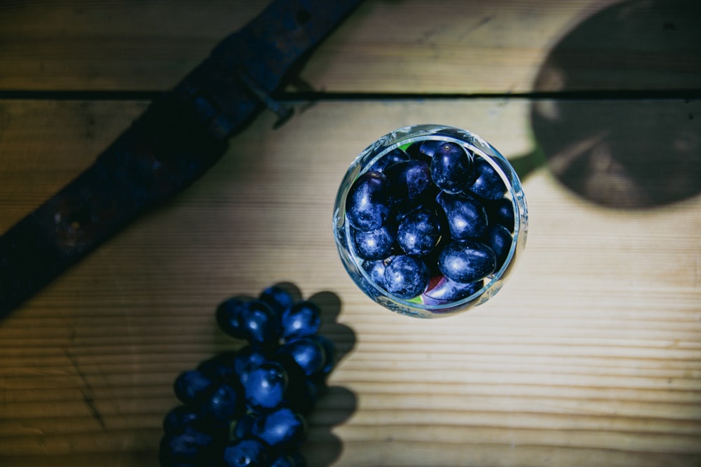 a glass filled with blue grapes on top of a wooden table