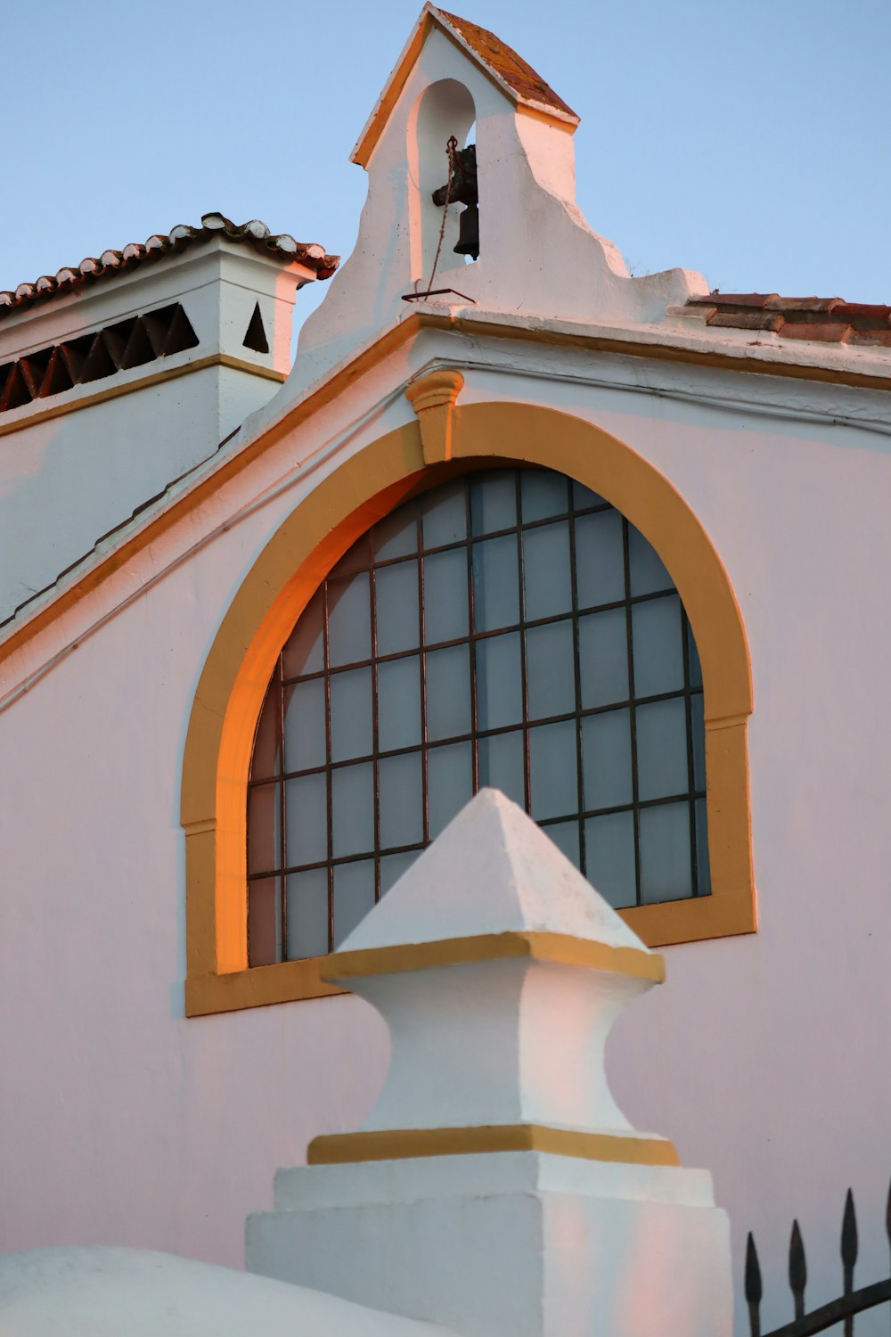 a white building with a yellow window and a black fence