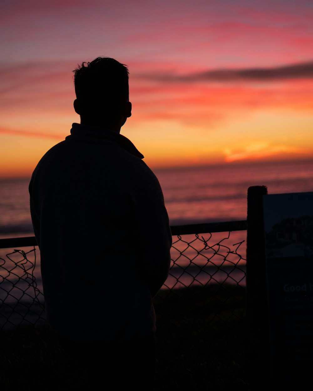 a man standing next to a fence near the ocean