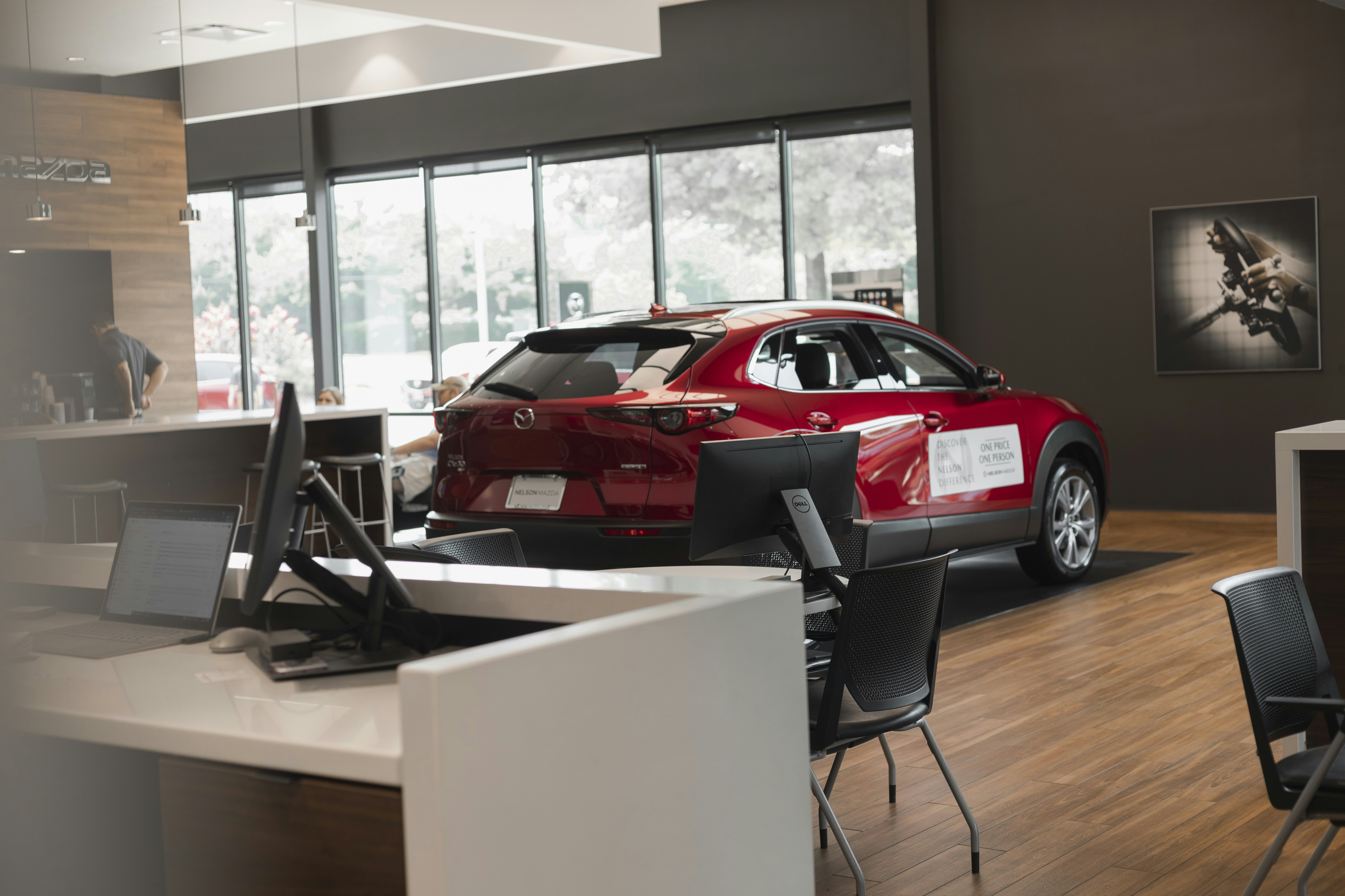 Photograph of the inside of a car dealership, with a red Mazda in the background and a desk in the foregroun