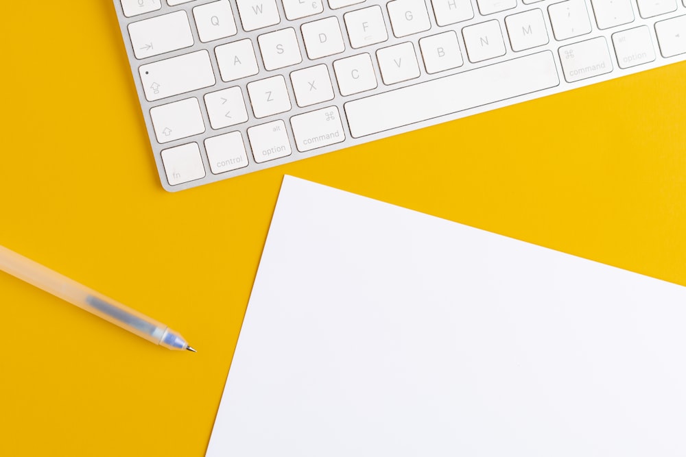eine Tastatur, eine Maus und ein Blatt Papier auf gelbem Hintergrund