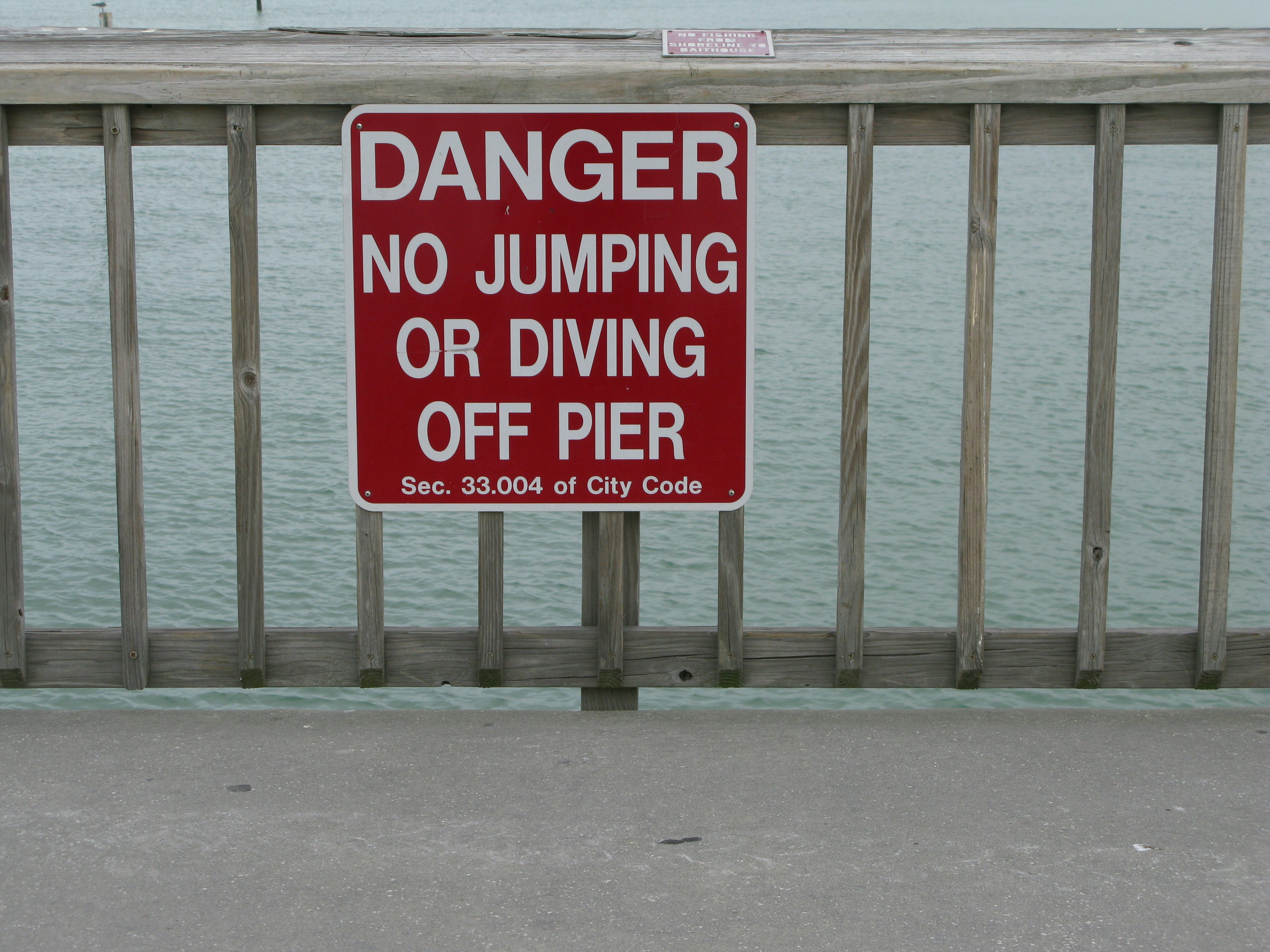 a red danger sign on a fence by a body of water