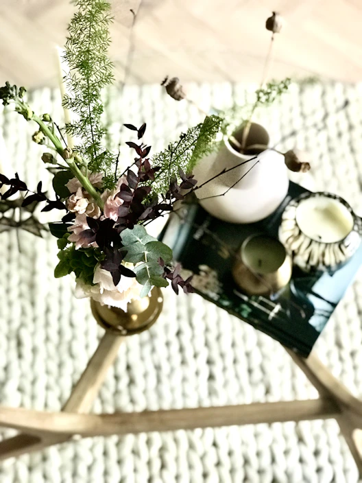 A cozy setup featuring stylish home decor pieces like candles, cushions, and plants on a wooden table with soft natural light.
