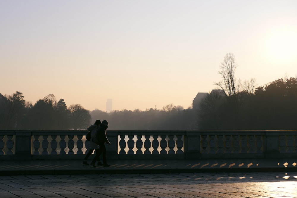 two people walking across a bridge at sunset