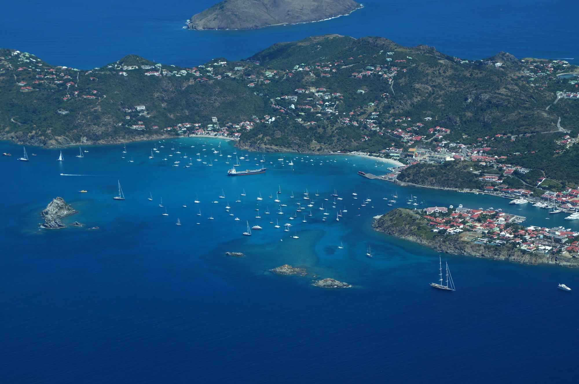 Aerial view of a green Caribbean island and a bay full of moored yachts, the end point of a private jet to the Caribbean