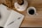 A notebook with lined pages labeled 'Reflection' lies open on a wooden table, with a pen resting on its pages. Nearby, there is a white ceramic mug filled with black coffee. Some dried flowers in a white vase are also present on the table.