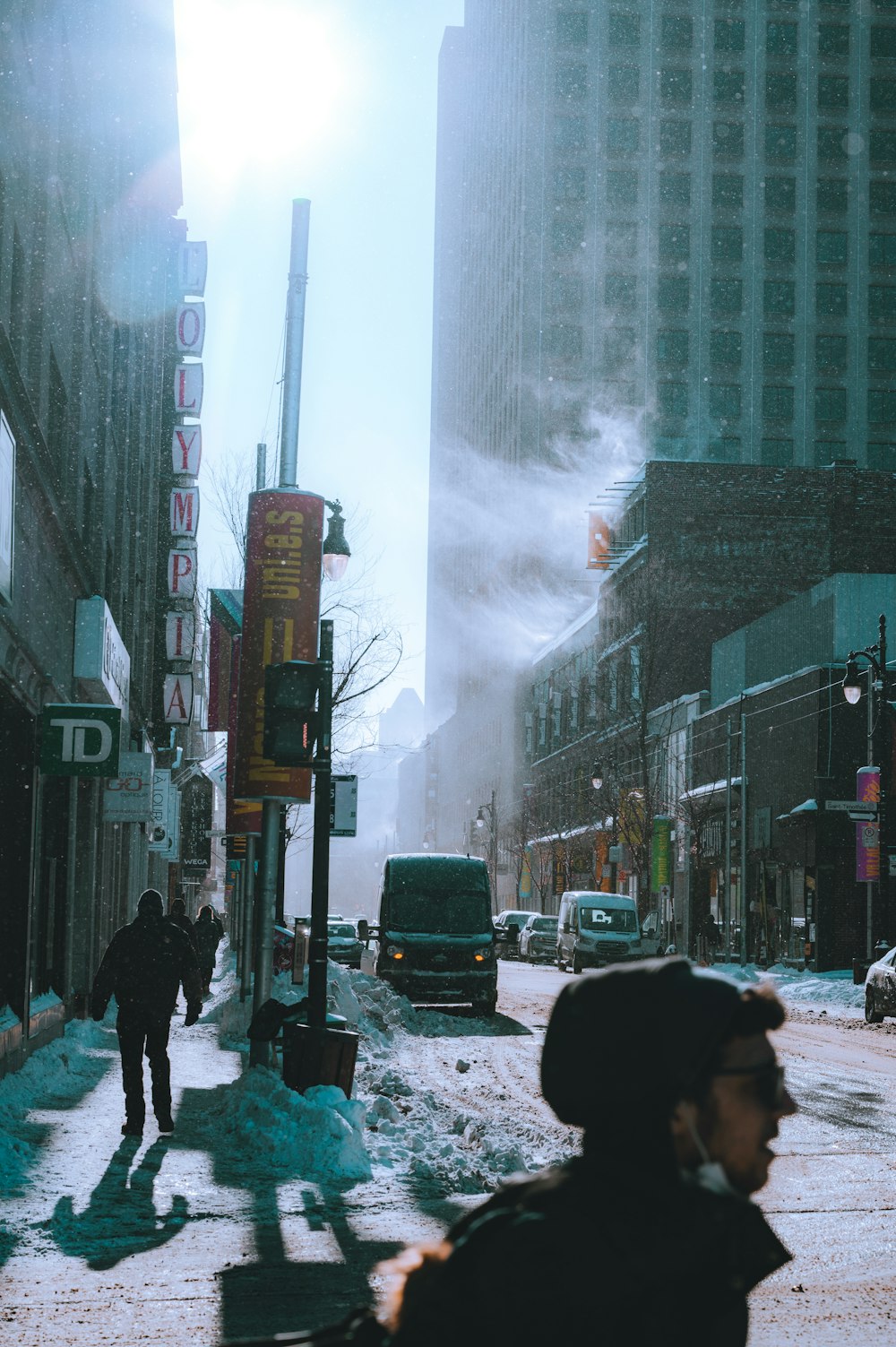 a man walking down a snow covered street next to tall buildings