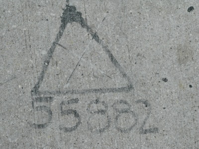 A triangle shape and the number 5582 drawn on a concrete surface, using a dark material on a light grey, textured background.