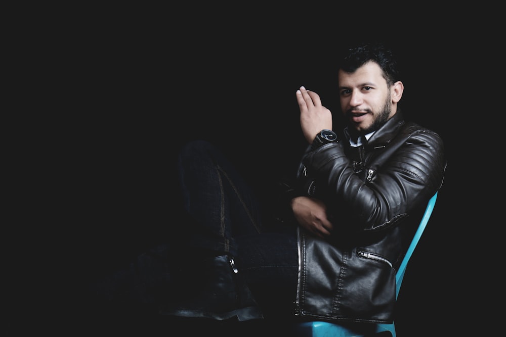 a man in a leather jacket sitting on a chair
