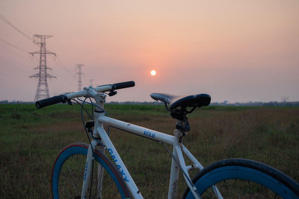 a bike parked in a field with the sun setting in the background