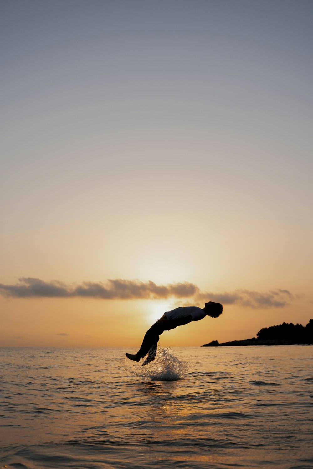 a person jumping into the water at sunset