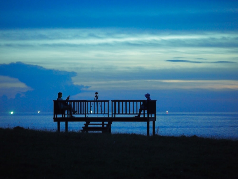 two people sitting on a bench overlooking the ocean