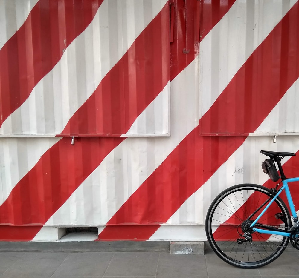 a blue bicycle parked next to a red and white striped wall
