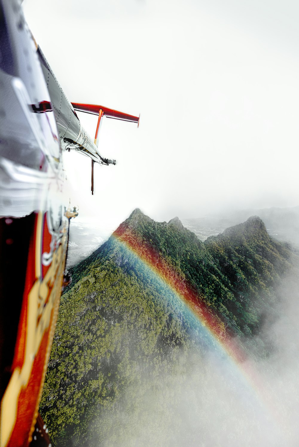 a helicopter flying over a mountain with a rainbow in the sky