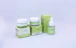 A set of skincare products with two jars and a dropper bottle placed in front of their respective boxes. The packaging is primarily green with white accents, and the brand and product names are visible on each container.