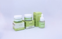 A set of skincare products with two jars and a dropper bottle placed in front of their respective boxes. The packaging is primarily green with white accents, and the brand and product names are visible on each container.