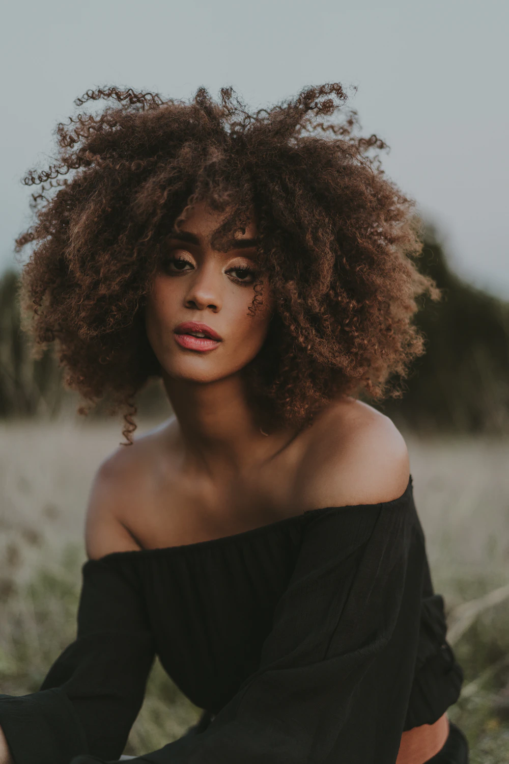 A woman with curly hair sitting outdoors in a field
