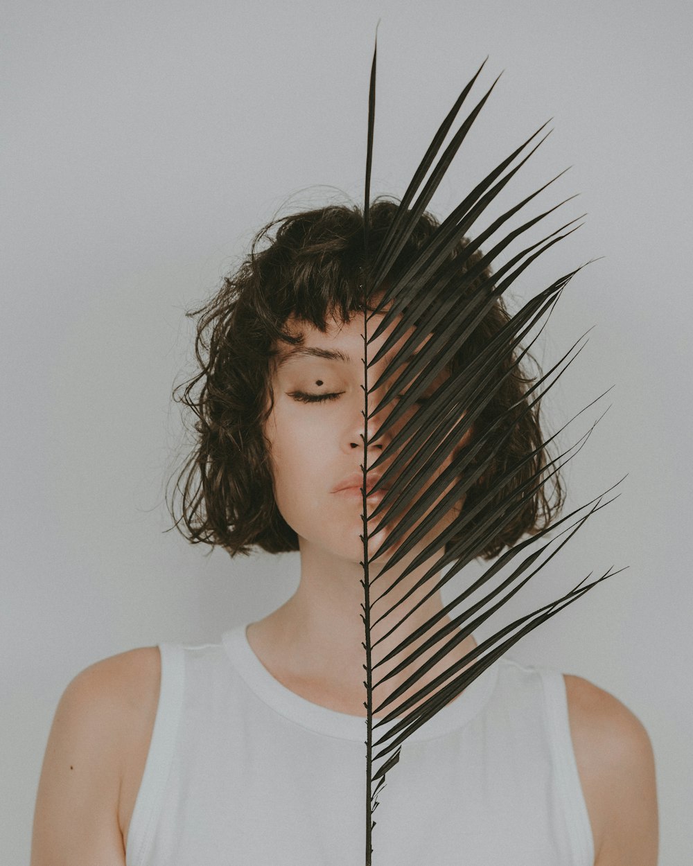 a woman with her eyes closed behind a palm leaf