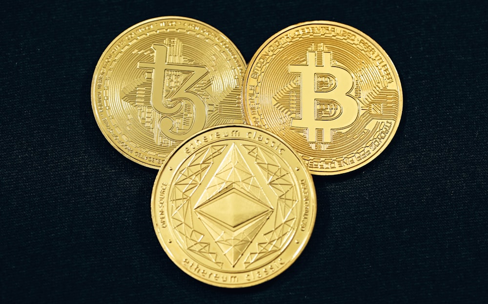 Drei goldene Bitcoins auf schwarzem Hintergrund