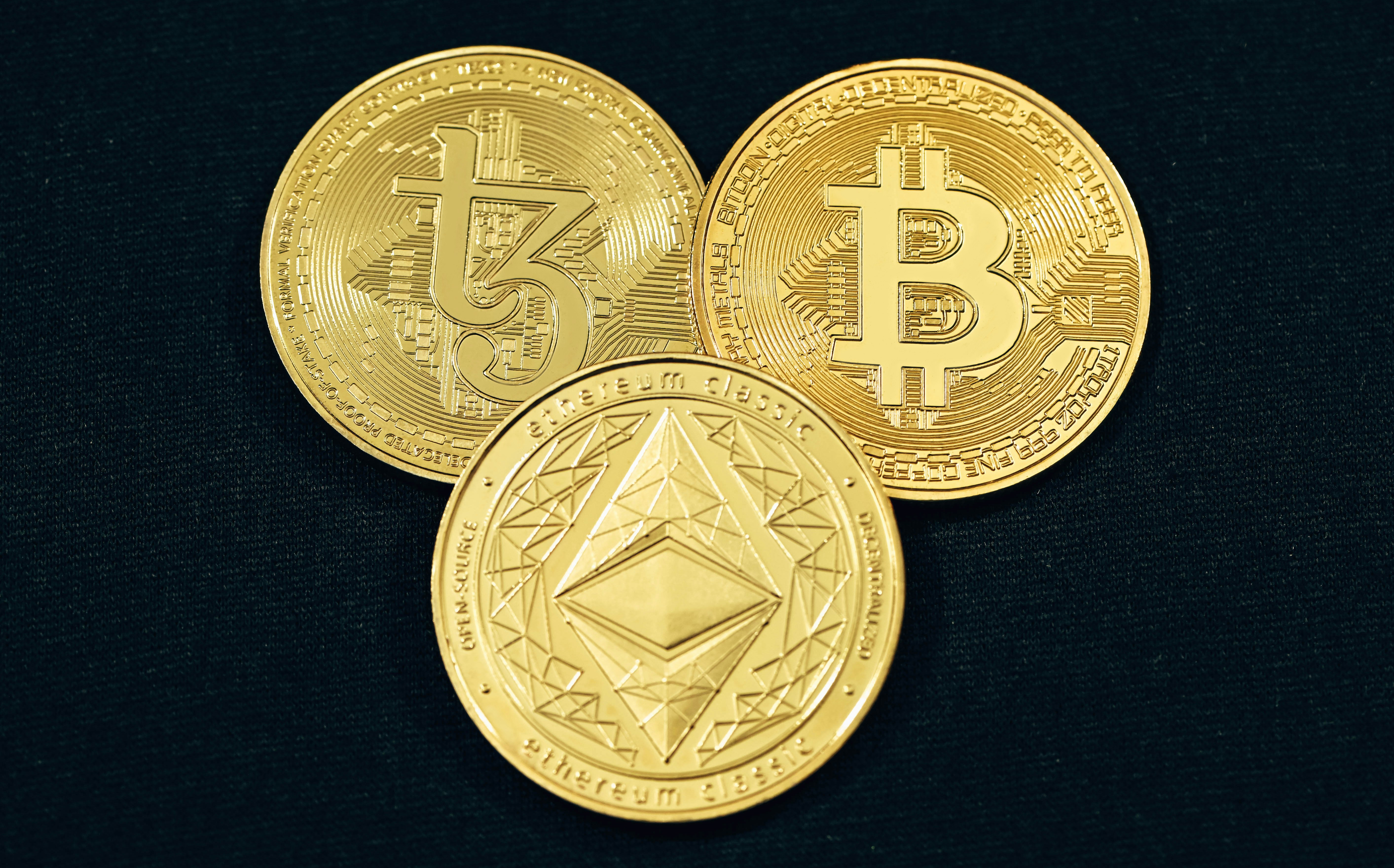Tezos, Bitcoin, and Ethereum placed on a black background