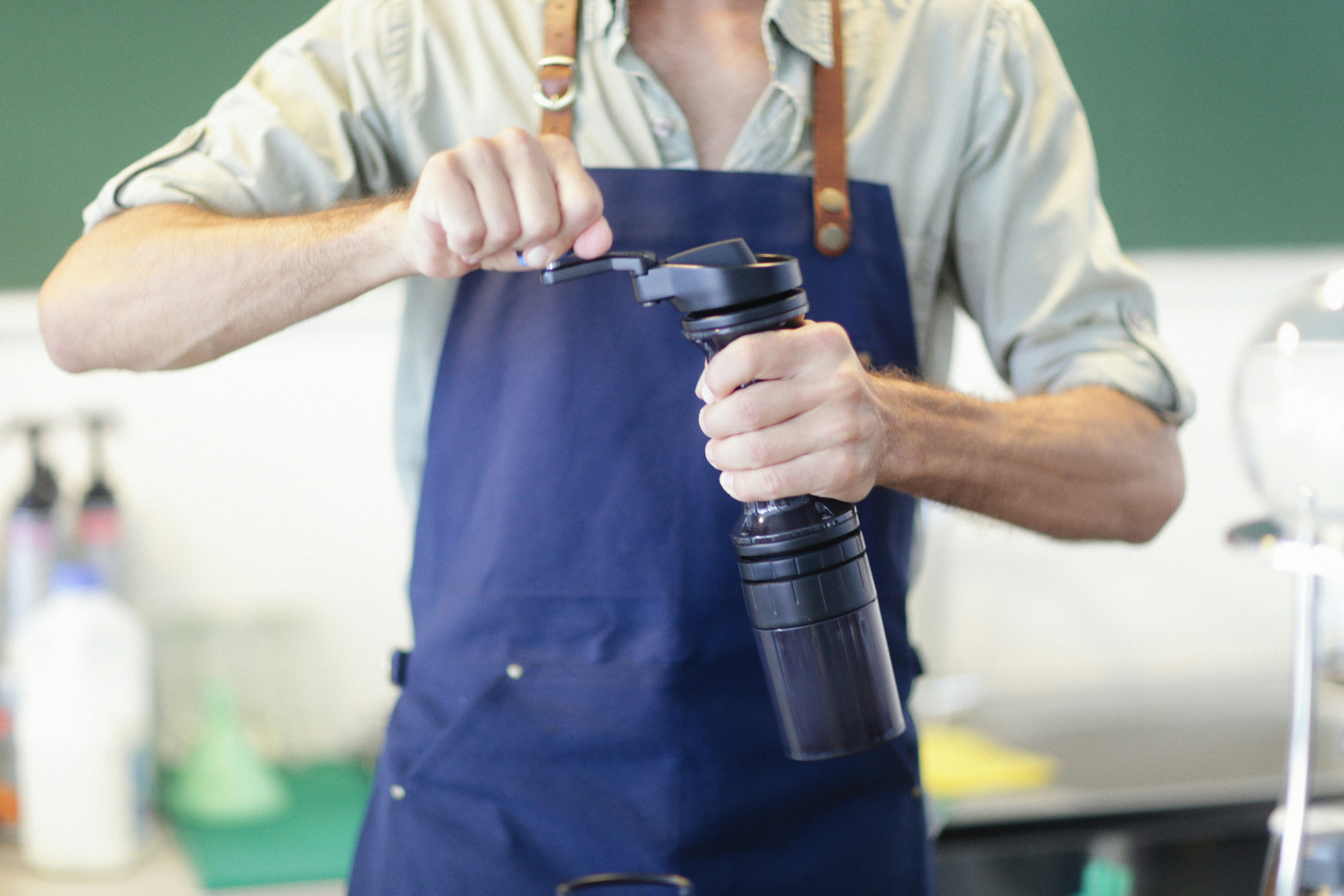 Barista in a blue apron holding a hand grinder