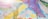 A canopy of vibrantly colored fabric panels stretches across the sky, featuring a variety of patterns including zigzags, florals, and abstract designs. Sunlight filters through the fabric, creating a bright and festive atmosphere.
