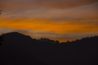 Sunset over the hills of Abujhmad with silhouettes of tribal huts and trees.
