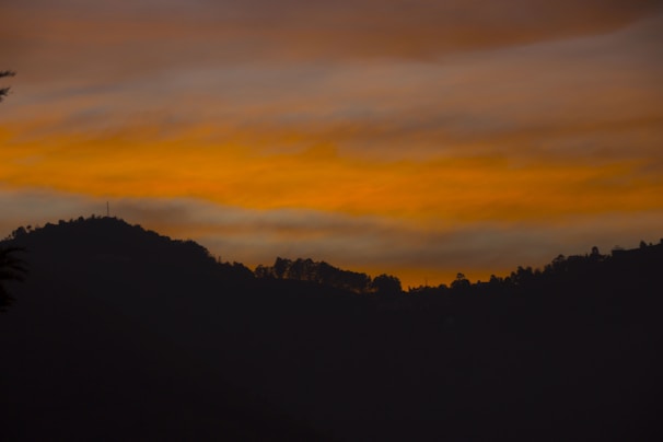 Sunset over the hills of Abujhmad with silhouettes of tribal huts and trees.