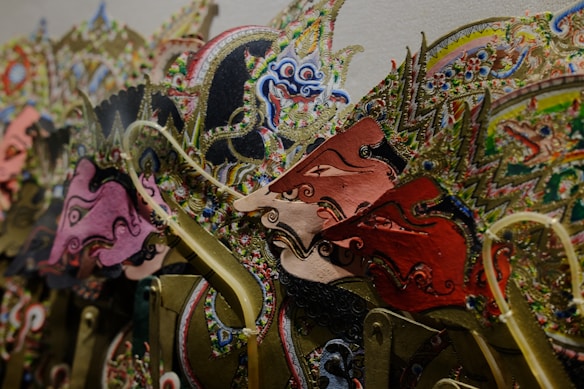 A collection of intricately designed puppets with colorful and detailed patterns. Each puppet has an ornate headdress and facial features, showcasing traditional artistic elements. The use of vibrant colors and meticulous detail highlights the craftsmanship involved.