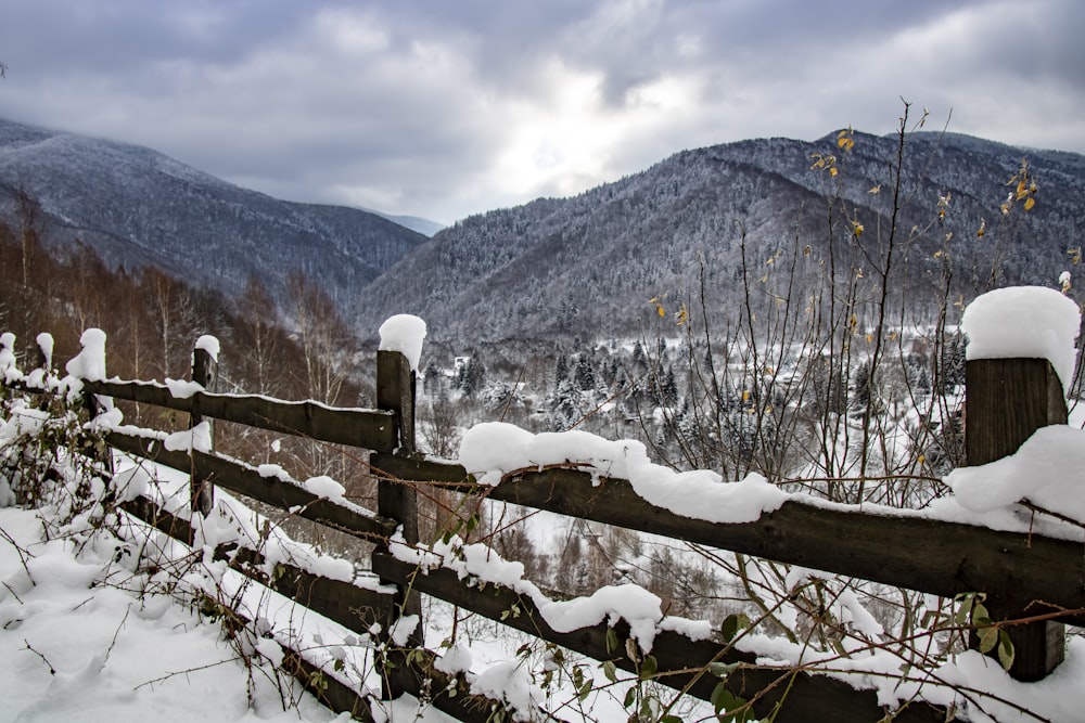 a wooden fence covered in snow next to a mountain