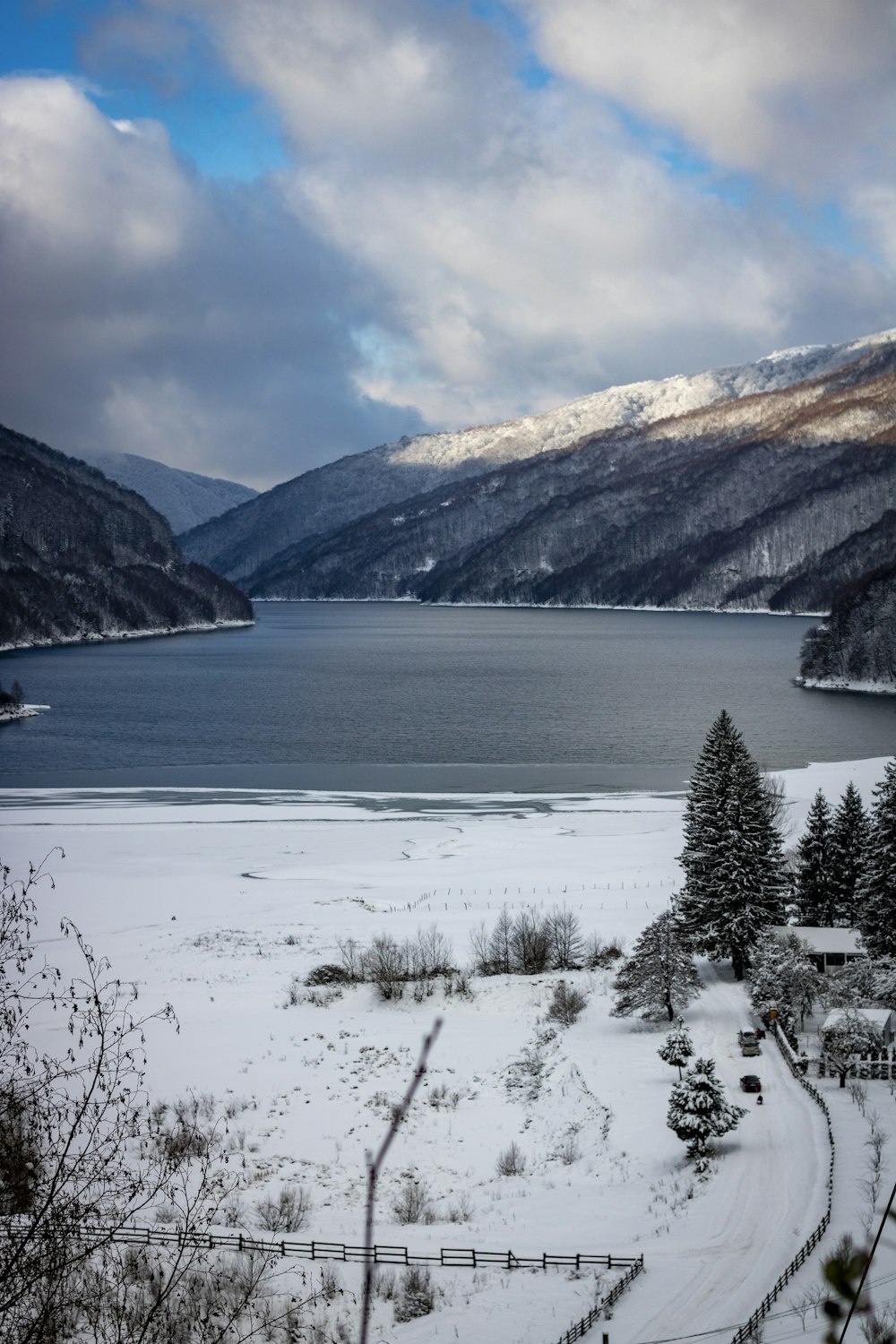 a lake surrounded by snow covered mountains under a cloudy sky