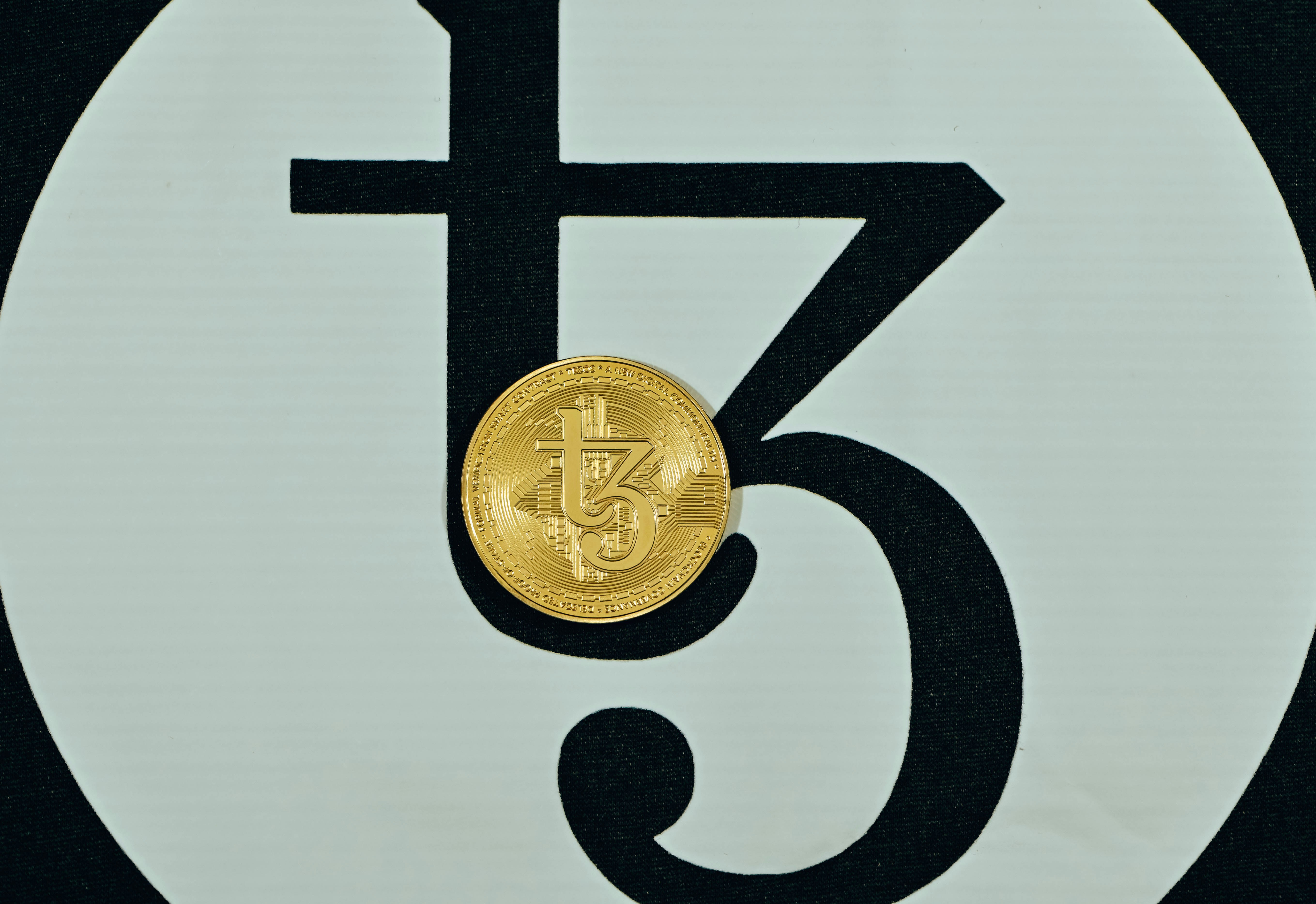 A gold Tezos coin placed on Tezos background