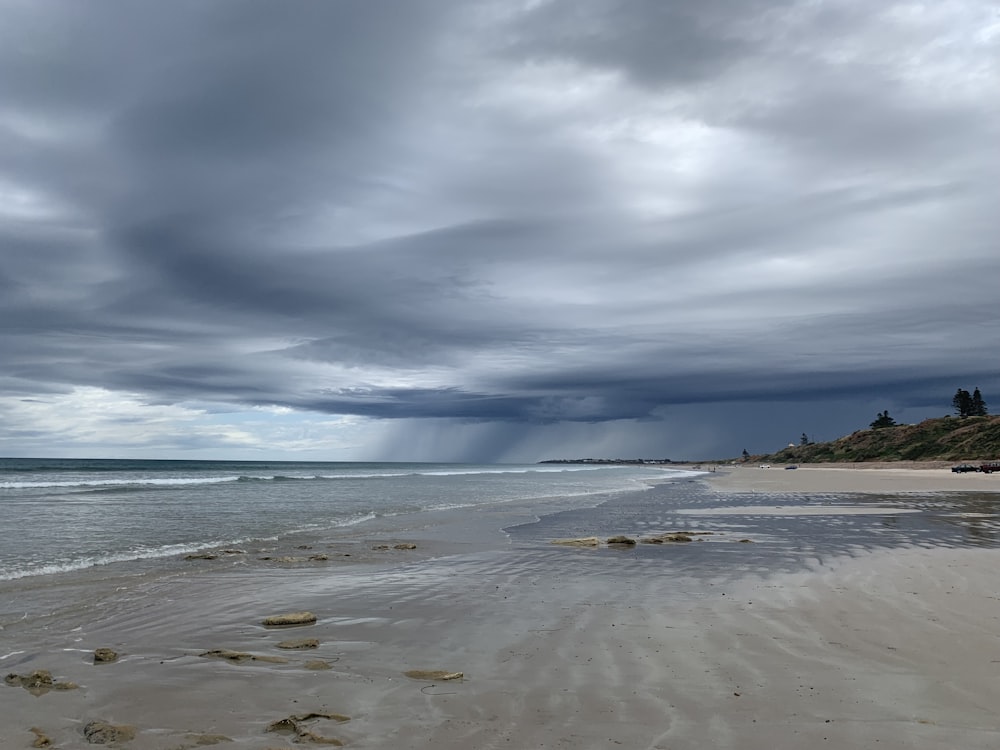 a sandy beach under a cloudy sky next to the ocean