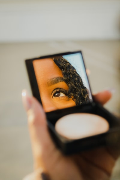 woman's reflection through a makeup mirror compact