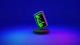 A smartphone displaying green computer code stands upright on a round, dark platform. The background fades from deep blue at the top to purple at the bottom, creating a futuristic and digital ambiance.