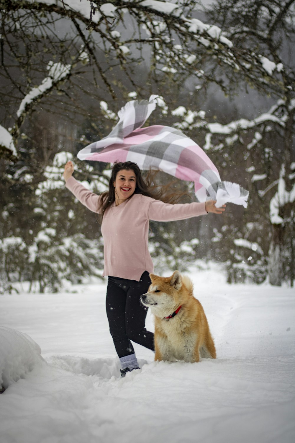 a woman standing in the snow with her dog