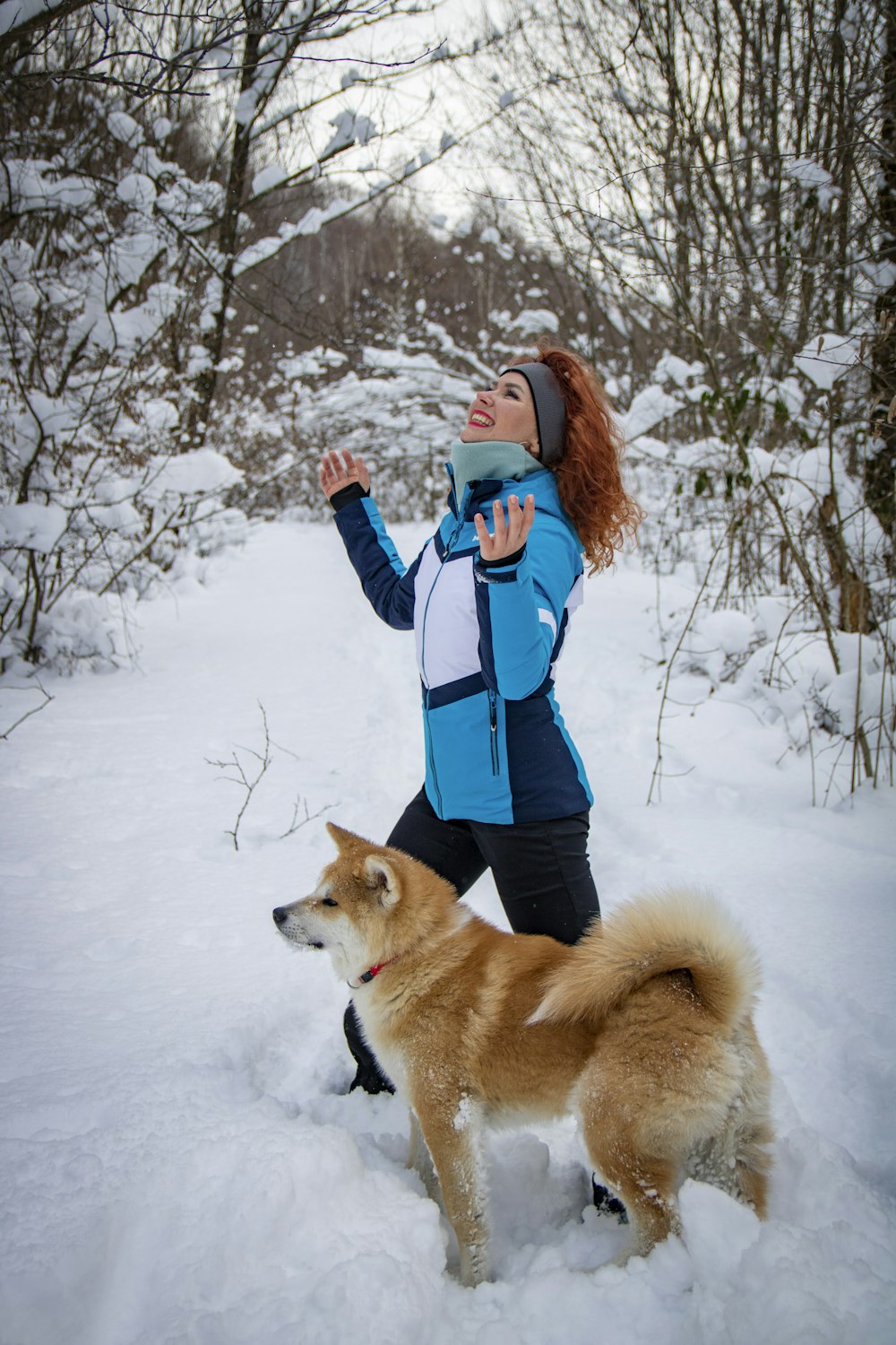 a woman in a blue and white jacket playing with a dog in the snow