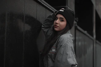 Model rocking a bandana and beanie combo, leaning against a graffiti-covered brick wall at dusk.