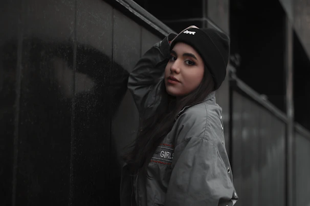 Model rocking a bandana and beanie combo, leaning against a graffiti-covered brick wall at dusk.