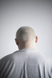 a man with a bald head standing in front of a white wall