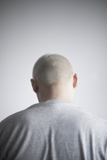 a man with a bald head standing in front of a white wall