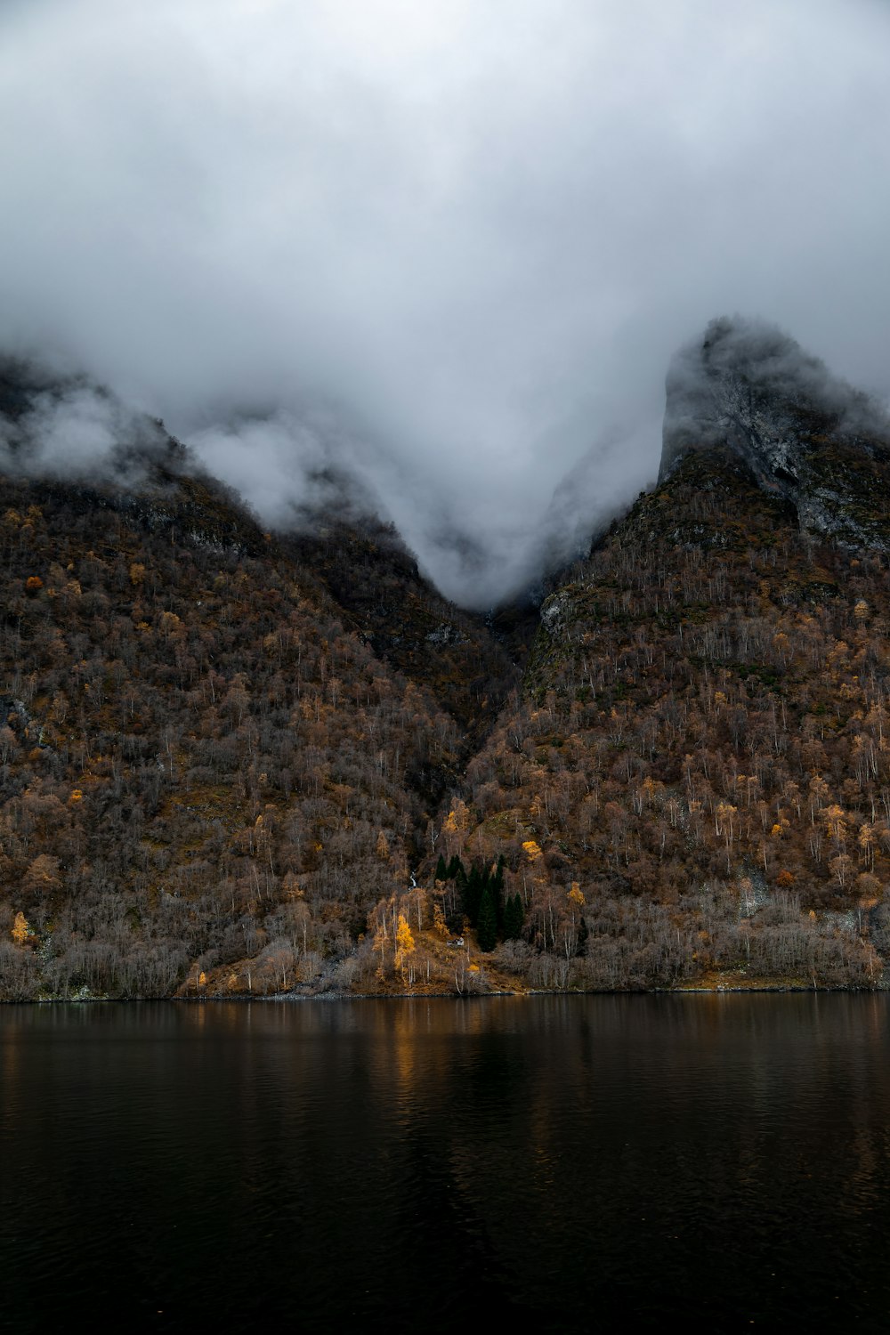 a mountain covered in clouds next to a body of water