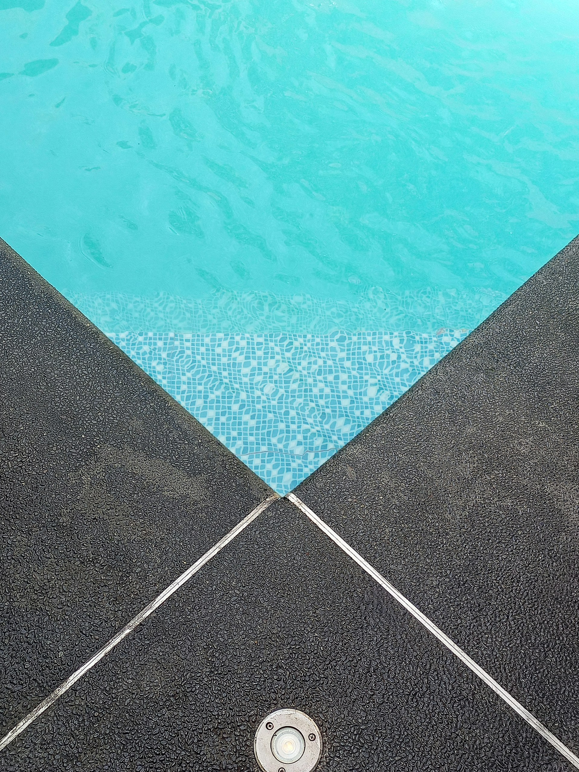 a blue swimming pool with a tile floor next to it
