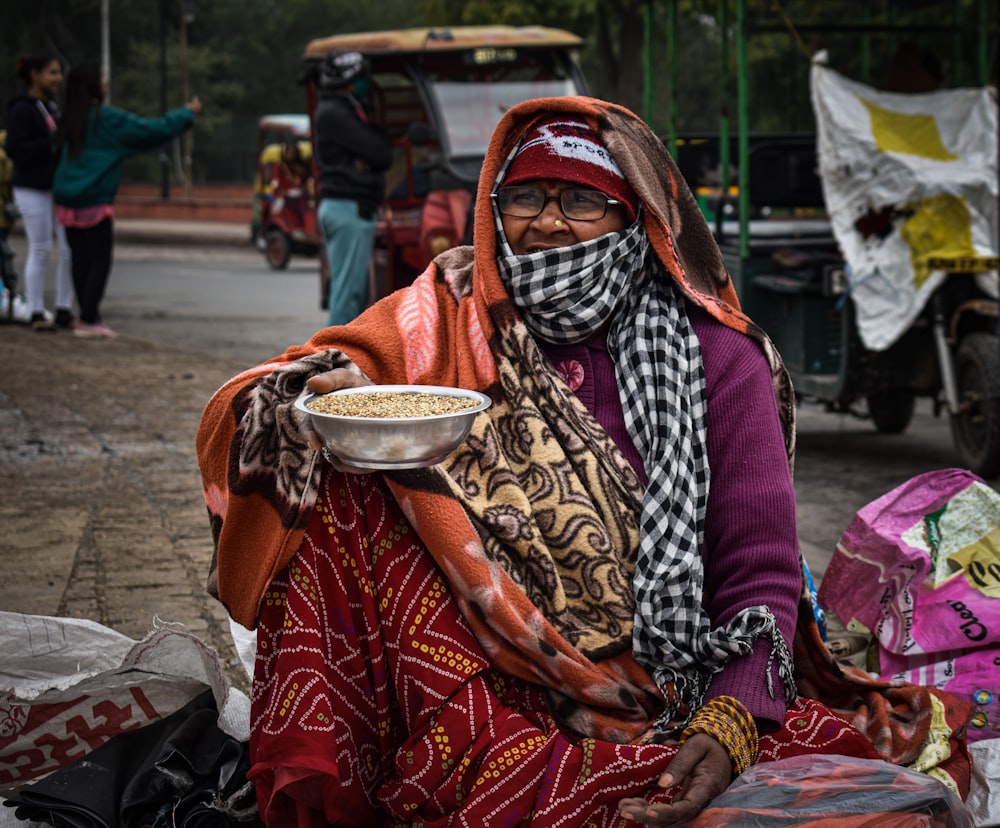 a woman sitting on the ground holding a bowl of food