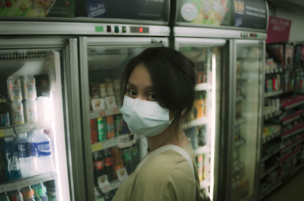 a woman wearing a face mask standing in front of a refrigerator