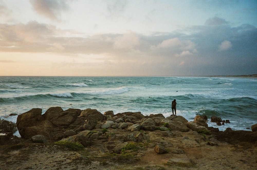 a person standing on a rocky beach next to the ocean