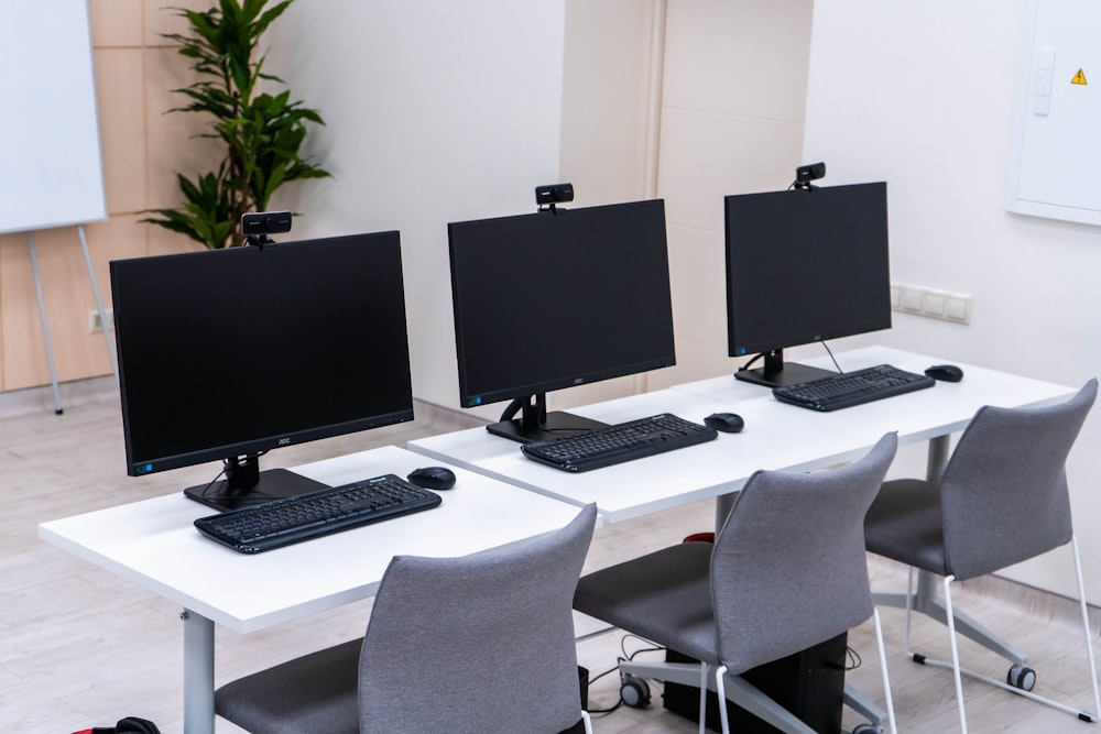 three computer monitors sitting on top of a white table